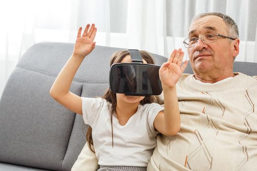 senior Caucasian man at home in the living room on the couch, grandfather and granddaughter with virtual glasses