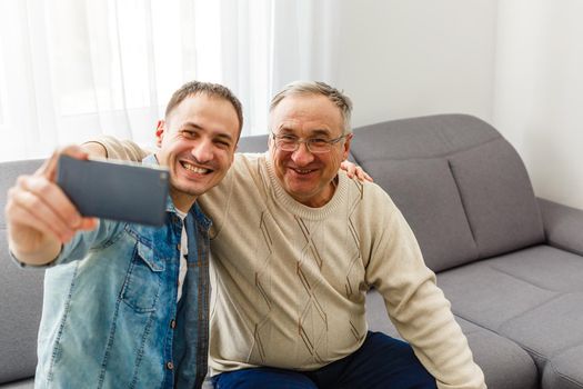 Smiling grown son sit on couch relax with senior dad talk sharing thoughts looking in eyes, happy millennial man rest on sofa speak with elderly father enjoy leisure family weekend at home