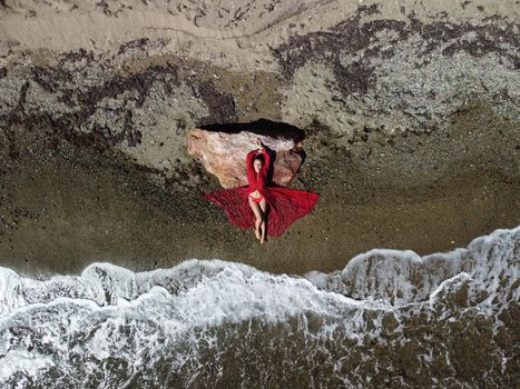 Young sensual blonde woman sitting on the rock near water at sea and enjoys the sea waves on background of two volcanic rocks, like in Iceland. Dreams holidays and weekend vacation in summer time