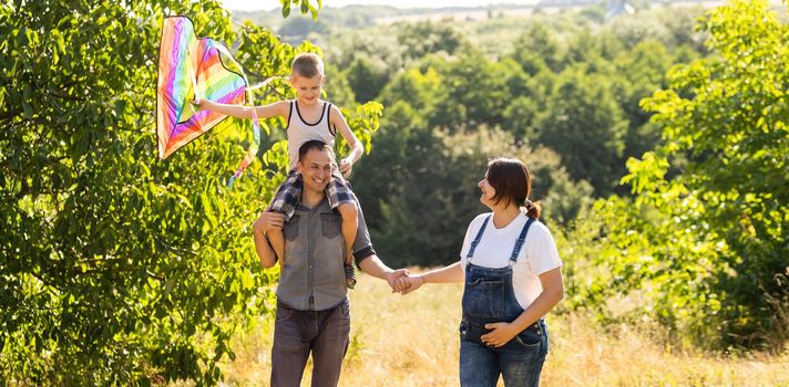 Happy family with pregnant wife fly a kite together in summer field