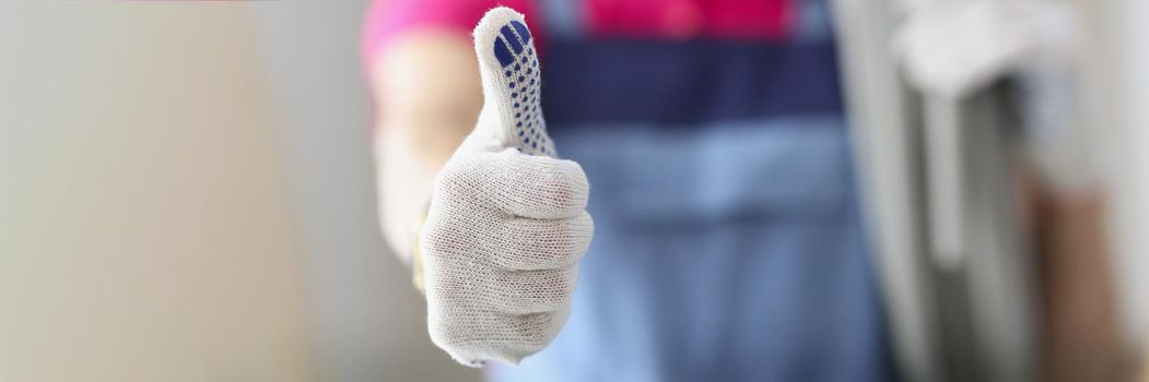 Close-up of woman hand demonstrating thumb up sign. Female repairer in coveralls. Motivational gesture. Repairs and renovation and repair home concept