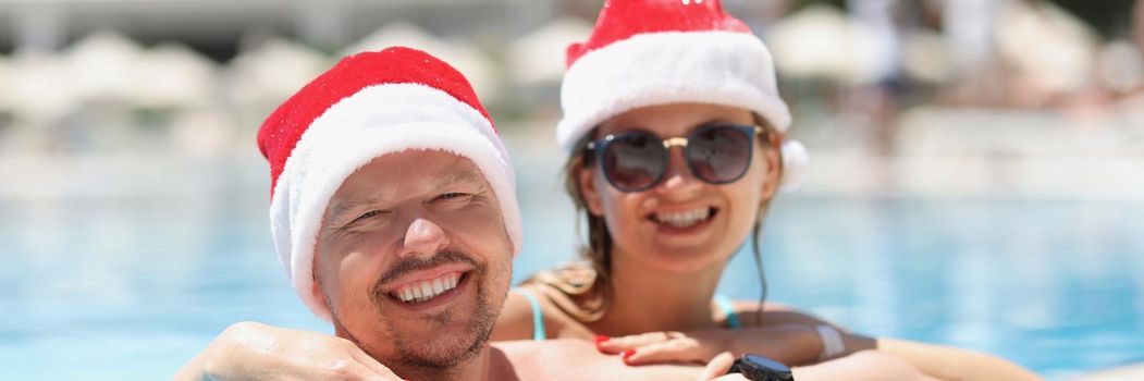 Portrait of happy couple posing for picture, memorable vacation in luxury resort, meet new year in exotic country. Wearing festive hats in swimming pool. Christmas, new year, holiday concept