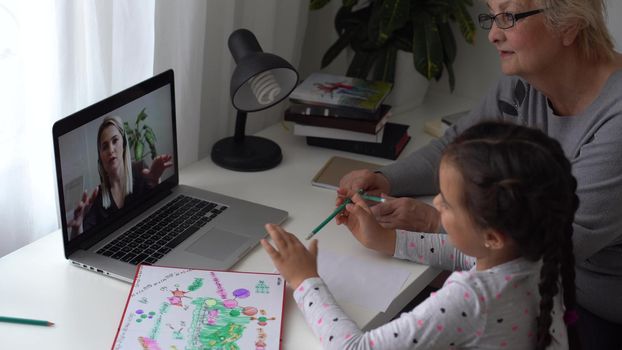 little girl studying with her grandmother at home, use laptop for education, online study, home studying. Girl has homework at distance learning. Lifestyle concept for Family quarantine covid-19.