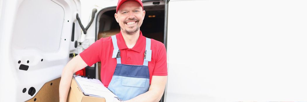 Portrait of joyful smiling guy from delivery service, man carry box and delivery receipt document on top. Come out truck with parcel. Shipping, dream job, courier concept