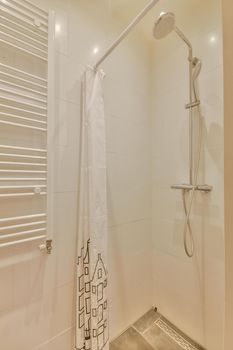 Shower faucets attached to tiled wall near glass partition and ornamental curtail in washroom at home