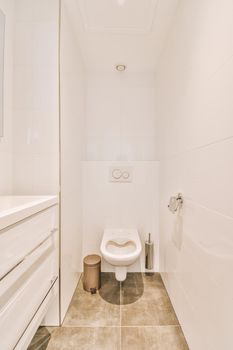 Interior of narrow restroom with sink and wall hung toilet with white walls and checkered floor