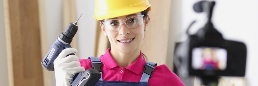Portrait of smiling woman in helmet holding screwdriver. Cheerful repairer blogger making video for building vlog. Renovation in apartment idea. Blogging and vlogging concept