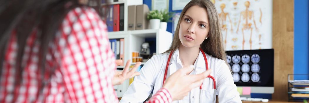 Portrait of serious female doctor listening carefully to patient. Young woman at doctor consultation in clinic office. Medicine and healthcare concept