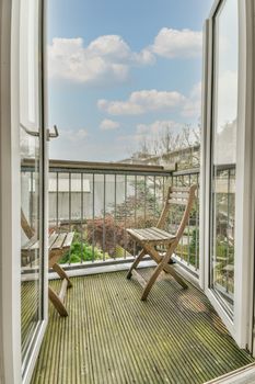 Narrow brick balcony with metal railings, wooden chair and door with glass leads to the kitchen