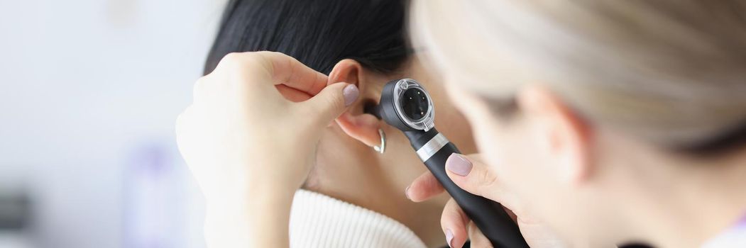 Close-up of female otolaryngologist examining ear with otoscope. Patient with earache at doctor appointment. Otolaryngology, medicine and healthcare concept
