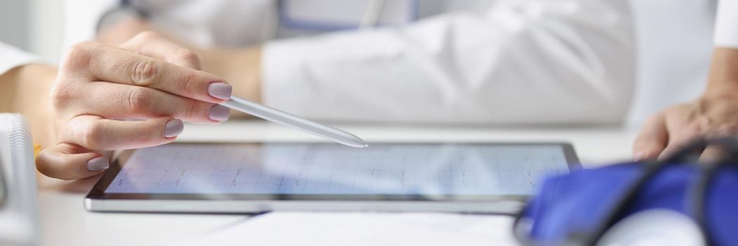 Close-up of woman practitioner showing cardiogram of patient to colleague. Physician using modern tablet. Online application for doctors. Modern diagnostics technologies concept