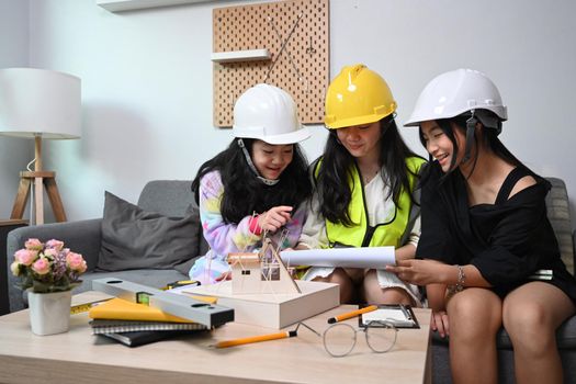 Three asian girls wearing hard hat while playing as engineer together at home.