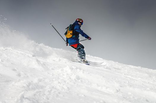 Freeride, a man is stylishly skiing on a snowy slope with snow dust plume behind him.