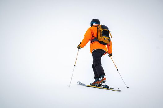 Winter skitour freeride in cloudy weather, snow-capped mountains against the backdrop of a glacier. Skier man in full gear climbs uphill in a skitour.