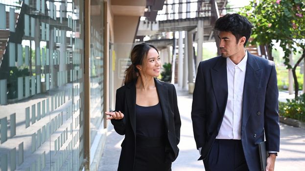 Two young business colleagues discussing business while walking outside office.