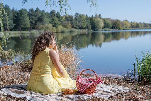 Leisure, free time. Beautiful caucasian woman in yellow dress on a picnic outdoors, sitting next to water