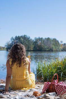 Leisure, free time. Beautiful caucasian woman in yellow dress on a picnic outdoors, sitting next to water