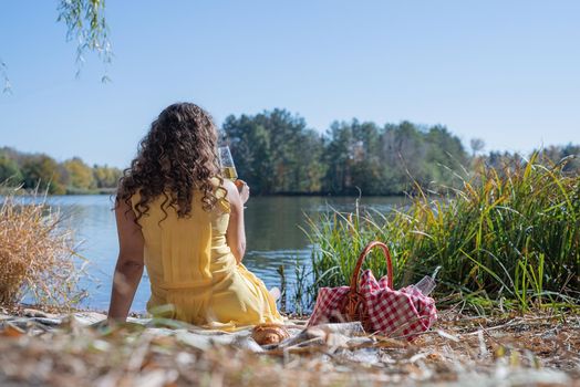 Leisure, free time. Beautiful caucasian woman in yellow dress on a picnic outdoors, sitting next to water