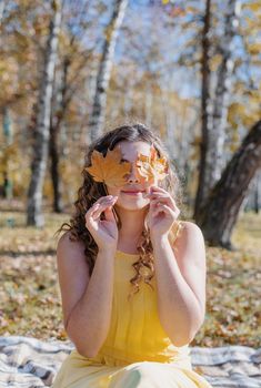 Leisure, free time. Beautiful caucasian woman in yellow dress on a picnic outdoors, sitting on a plaid in forest