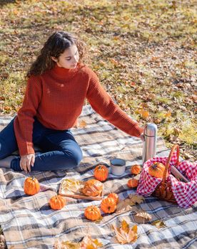 Leisure, free time. Beautiful caucasian woman in red sweater on a picnic outdoors, sitting on a plaid in autumn forest