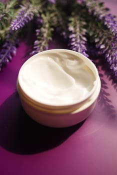 herbal cream cosmetic in a container and lavender flower on purple background .