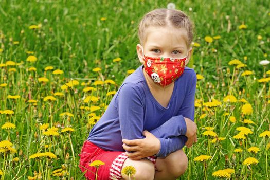 Caucasian little girl wearing mask on face to prevent from pollen allergy on dandelion lawn