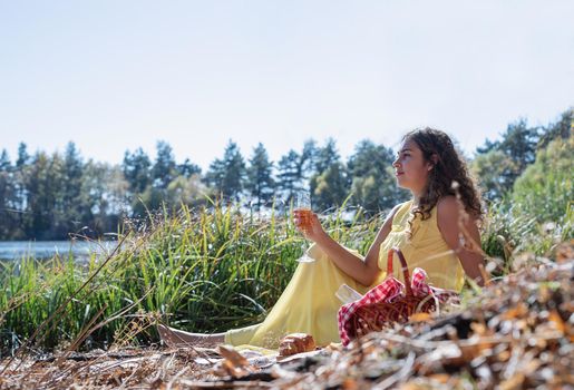 Leisure, free time. Beautiful caucasian woman in yellow dress on a picnic outdoors, sitting next to water