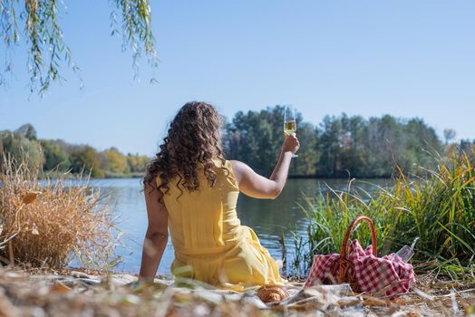 Leisure, free time. Beautiful caucasian woman in yellow dress on a picnic outdoors, sitting next to water