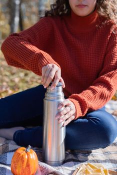 Leisure, free time. Beautiful caucasian woman in red sweater on a picnic outdoors, sitting on a plaid in autumn forest