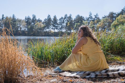 Leisure, free time. Beautiful caucasian woman in yellow dress on a picnic outdoors, sitting next to water