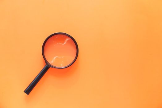 top view of magnifying glass on orange background .