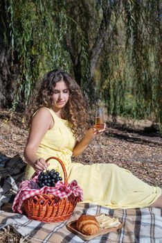 Leisure, free time. Beautiful caucasian woman in yellow dress on a picnic outdoors, sitting next to water