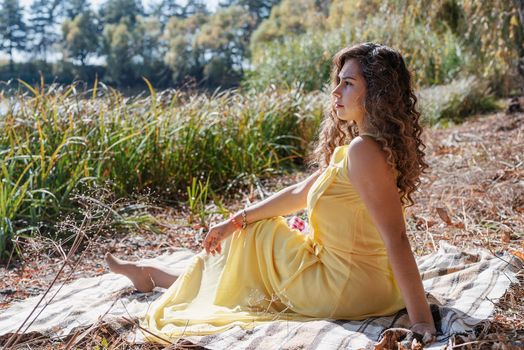 Leisure, free time. Beautiful caucasian woman in yellow dress on a picnic outdoors, sitting next to water