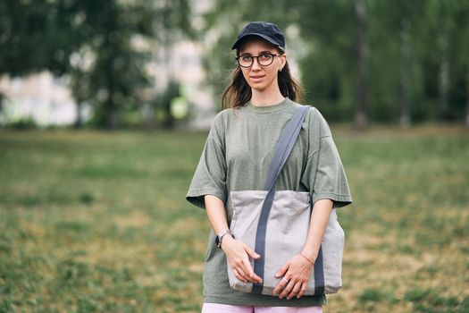Young woman with glasses holding empty cotton eco bag, mockup design. High quality photo