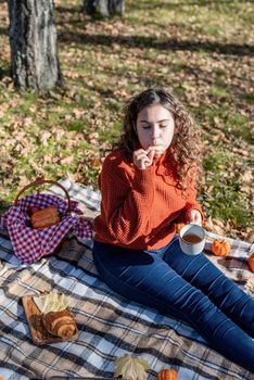 Leisure, free time. Beautiful caucasian woman in red sweater on a picnic outdoors, sitting on a plaid in autumn forest