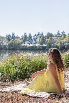 Leisure, free time. Beautiful caucasian woman in yellow dress on a picnic outdoors, sitting next to water