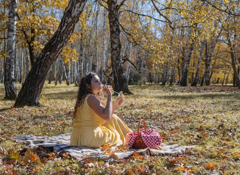 Leisure, free time. Beautiful caucasian woman in yellow dress on a picnic outdoors, sitting on a plaid in forest