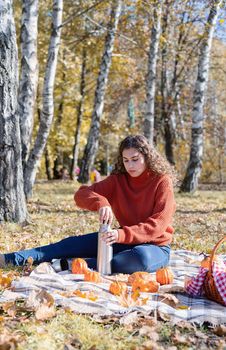 Leisure, free time. Beautiful caucasian woman in red sweater on a picnic outdoors, sitting on a plaid in autumn forest