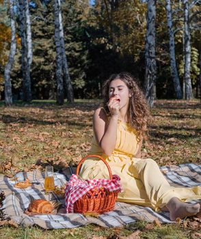 Leisure, free time. Beautiful caucasian woman in yellow dress on a picnic outdoors, sitting on a plaid in forest