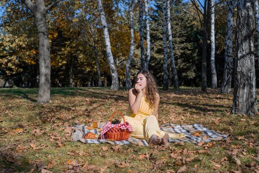 Leisure, free time. Beautiful caucasian woman in yellow dress on a picnic outdoors, sitting on a plaid in forest