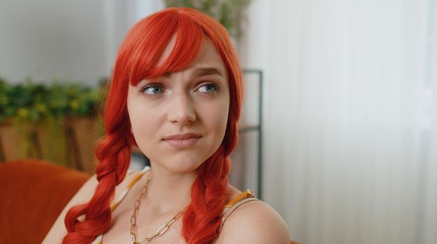 Close-up of sad young redhead woman sitting at home looks pensive thinks over life concerns or unrequited love, suffers from unfair situation. Problem, break up, depressed feeling bad annoyed, burnout