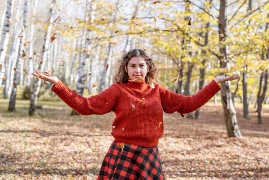 Autumn nature. Young happy woman in red sweater throwing leaves in autumn forest