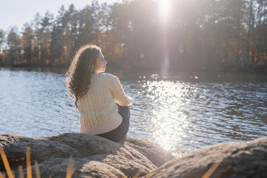 Freedom concept. Thoughtful romantic woman sitting on the river bank in sunset in autumn day