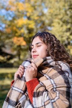 Autumn nature. Portrait of young happy woman in warm plaid in autumn forest