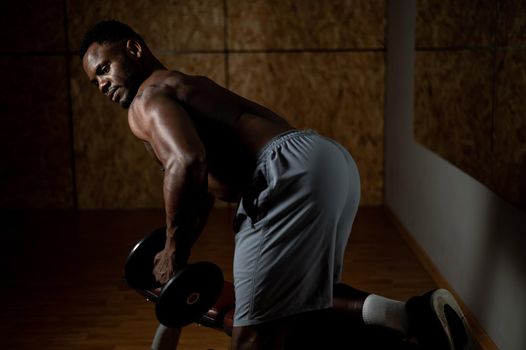 African american man with naked torso doing triceps row with dumbbell on bench