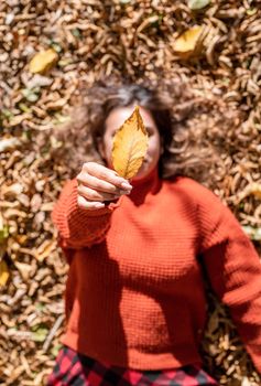 Autumn nature. Young happy woman in red sweater gathering leaves in autumn forest