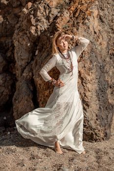 Middle aged woman looks good with blond hair, boho style in white long dress on the beach decorations on her neck and arms