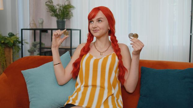 Woman freelancer hold three gold coins at home, successful developer programmer. Girl stock trader earning bitcoins after online monitoring trading operations. Increasing wealth, financial prosperity