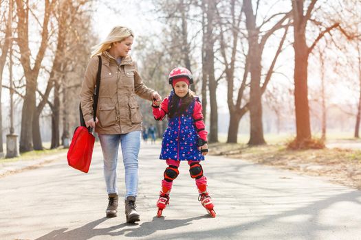 Mother and her daughter wearing roller skates in park.