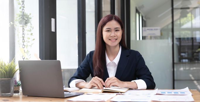 Charming Asian woman working at the office using a laptop Looking at the camera..